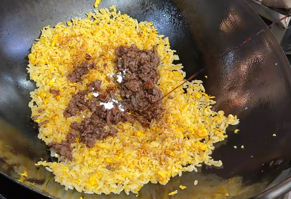 Cantonese-style egg fried rice with diced meat cooking in a wok