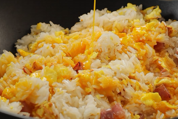 Beaten egg being poured over rice with diced ingredients in a wok