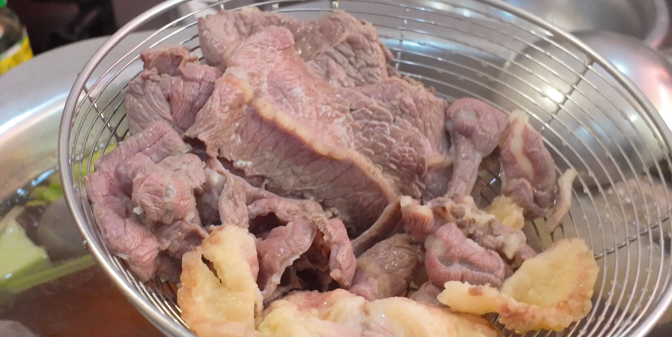 Cooked beef and beef pieces in a wire skimmer above hotpot broth