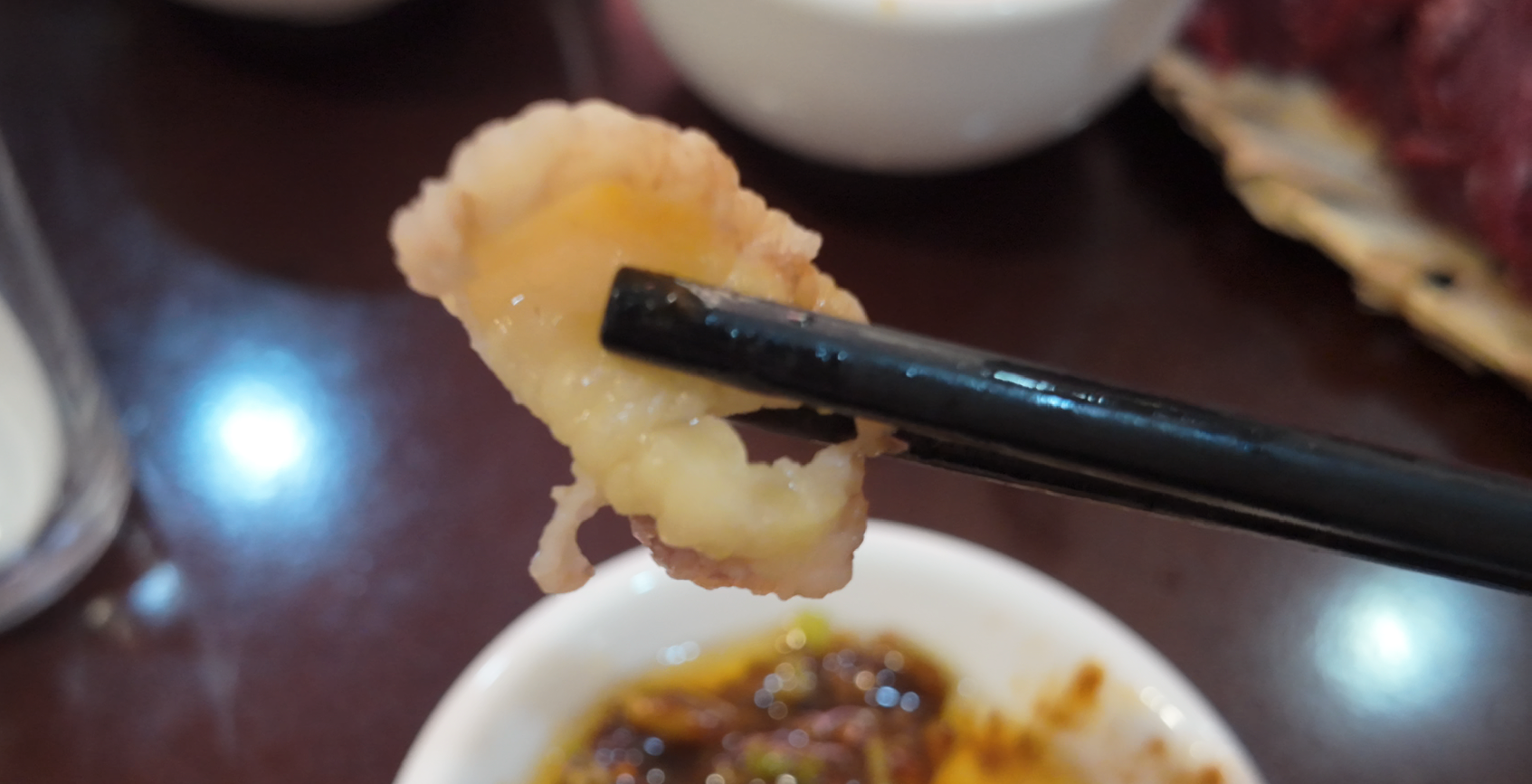 Cooked beef and fat held by chopsticks above a dipping bowl