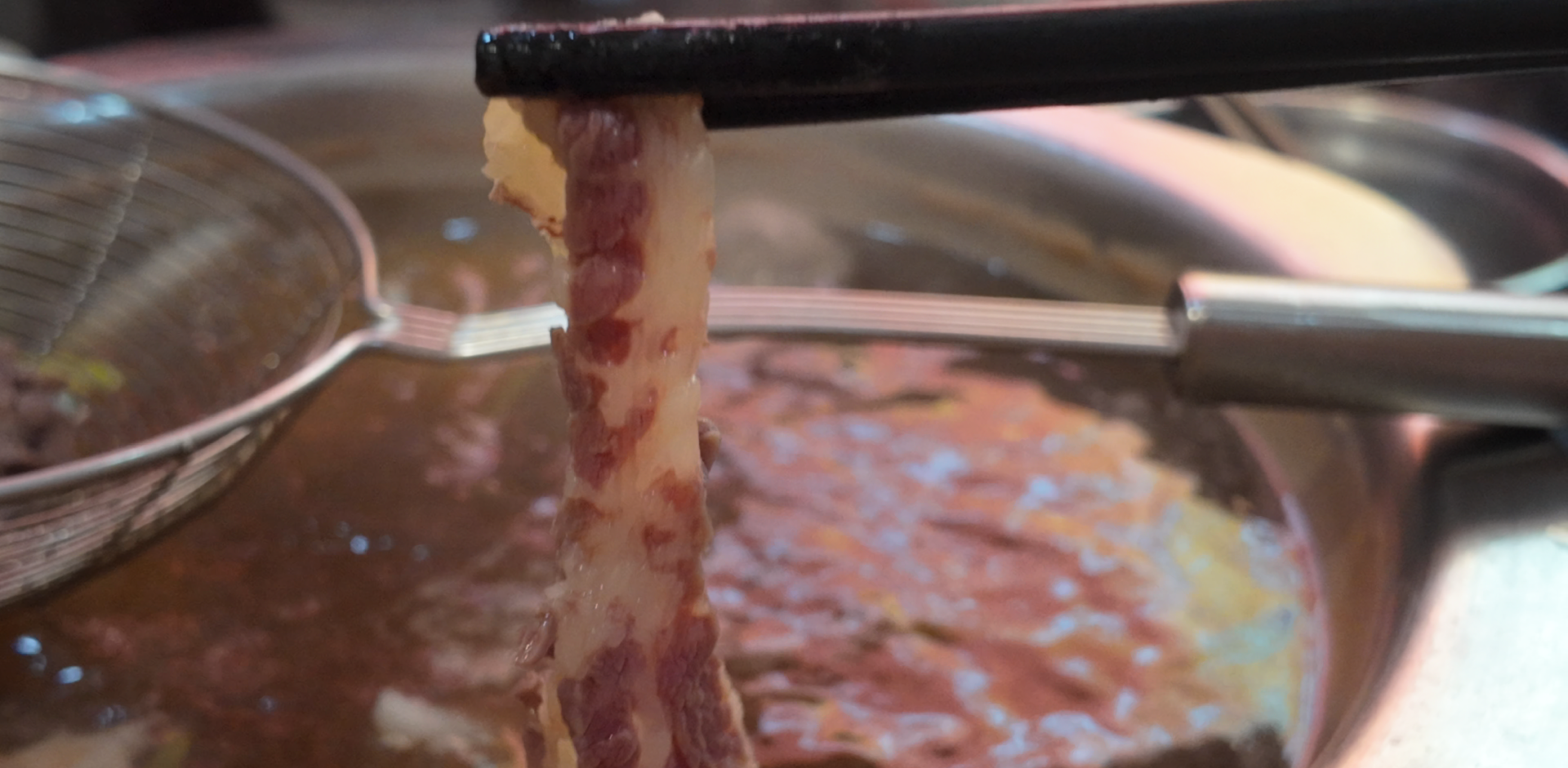 Thin slice of beef and fat held above hotpot broth